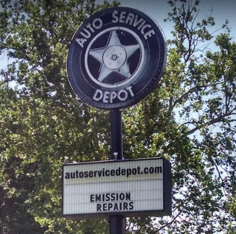 Screen Shot 2025-04-03 at 3.11.58 PM Vintage round Auto Service Depot sign with a five‑point wheel emblem mounted above a marquee reading "autoservicedepot.com" and "EMISSION REPAIRS," set against leafy trees
