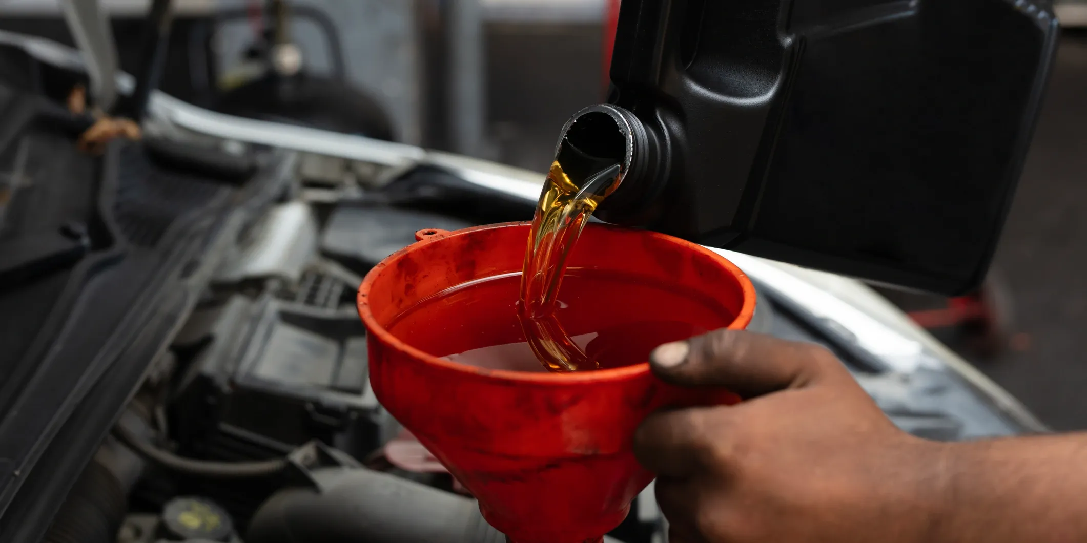 cr=t_12 Mechanic pouring fresh motor oil from a black jug through a red funnel into a car engine during an oil change at a family-owned auto repair shop in Tucker, GA